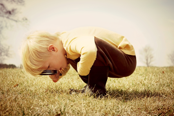 Young boy using a magnifying glass to look closely at the grass