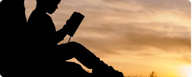 Person reading outdoors in silhouette at sunset