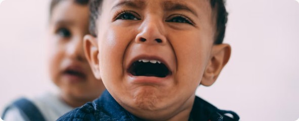 Young child crying while another child stands behind them
