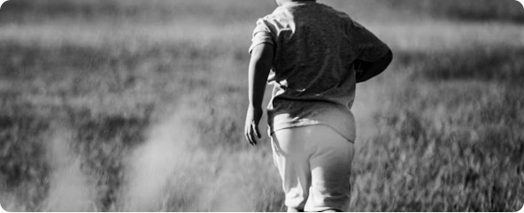 Child running through a field, photographed from behind